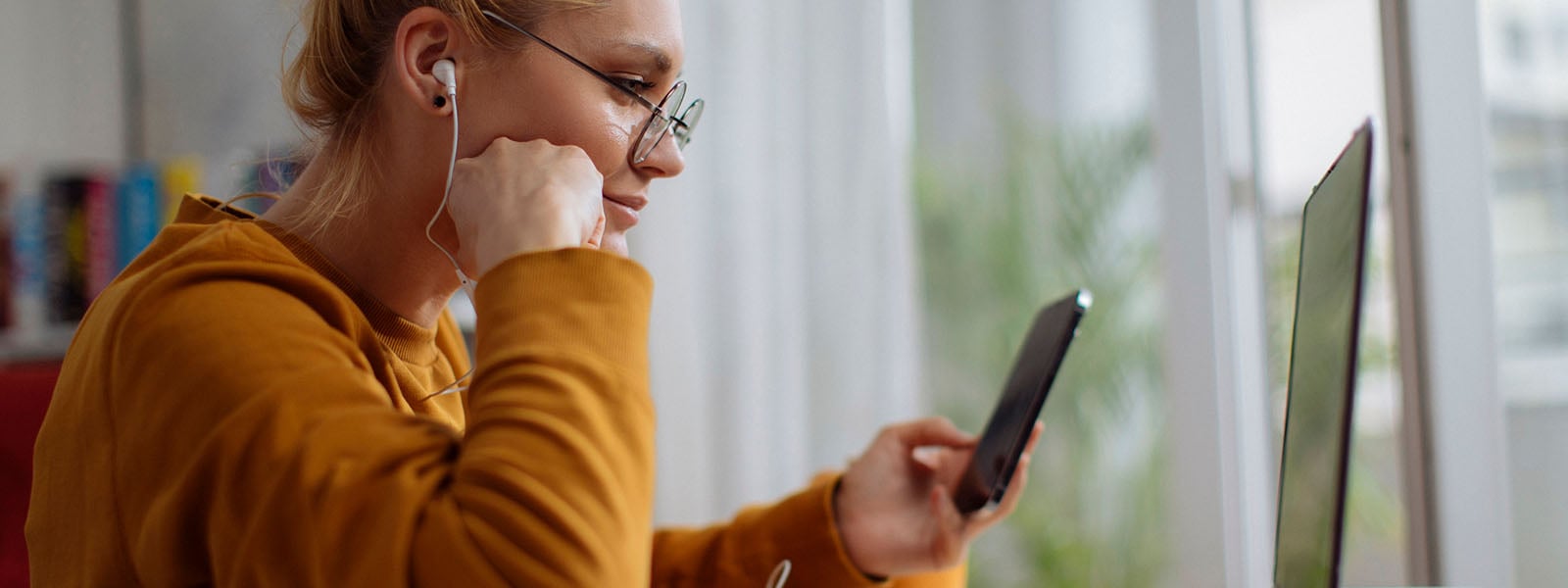 Une femme assise devant un ordinateur saisissant le code d'authentification à deux facteurs sur son téléphone.