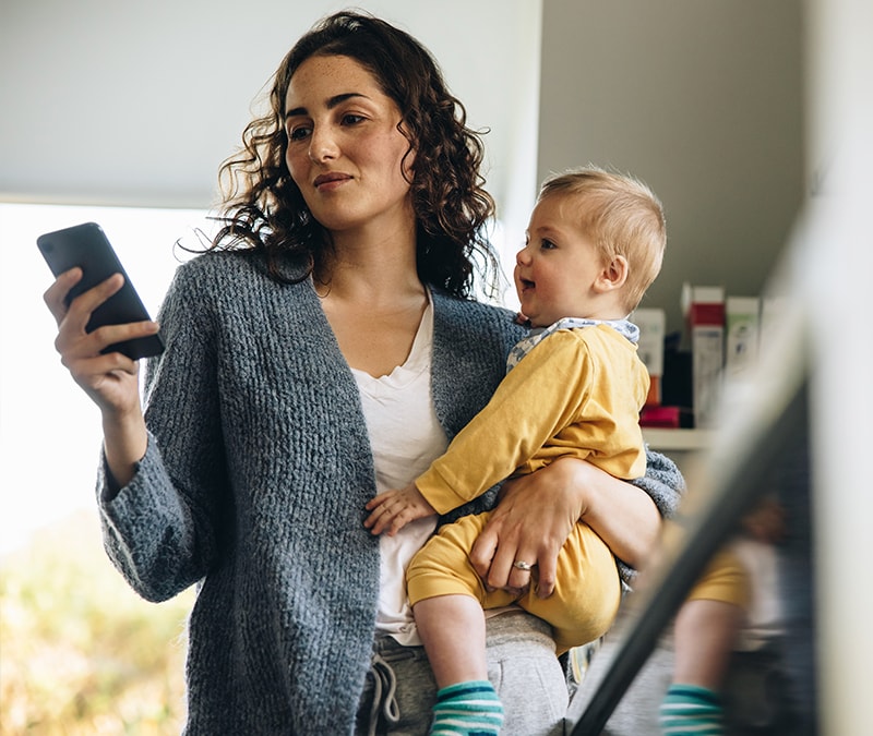 Une mère cherchant à éviter les escroqueries sur WhatsApp tout en tenant son enfant dans ses bras.